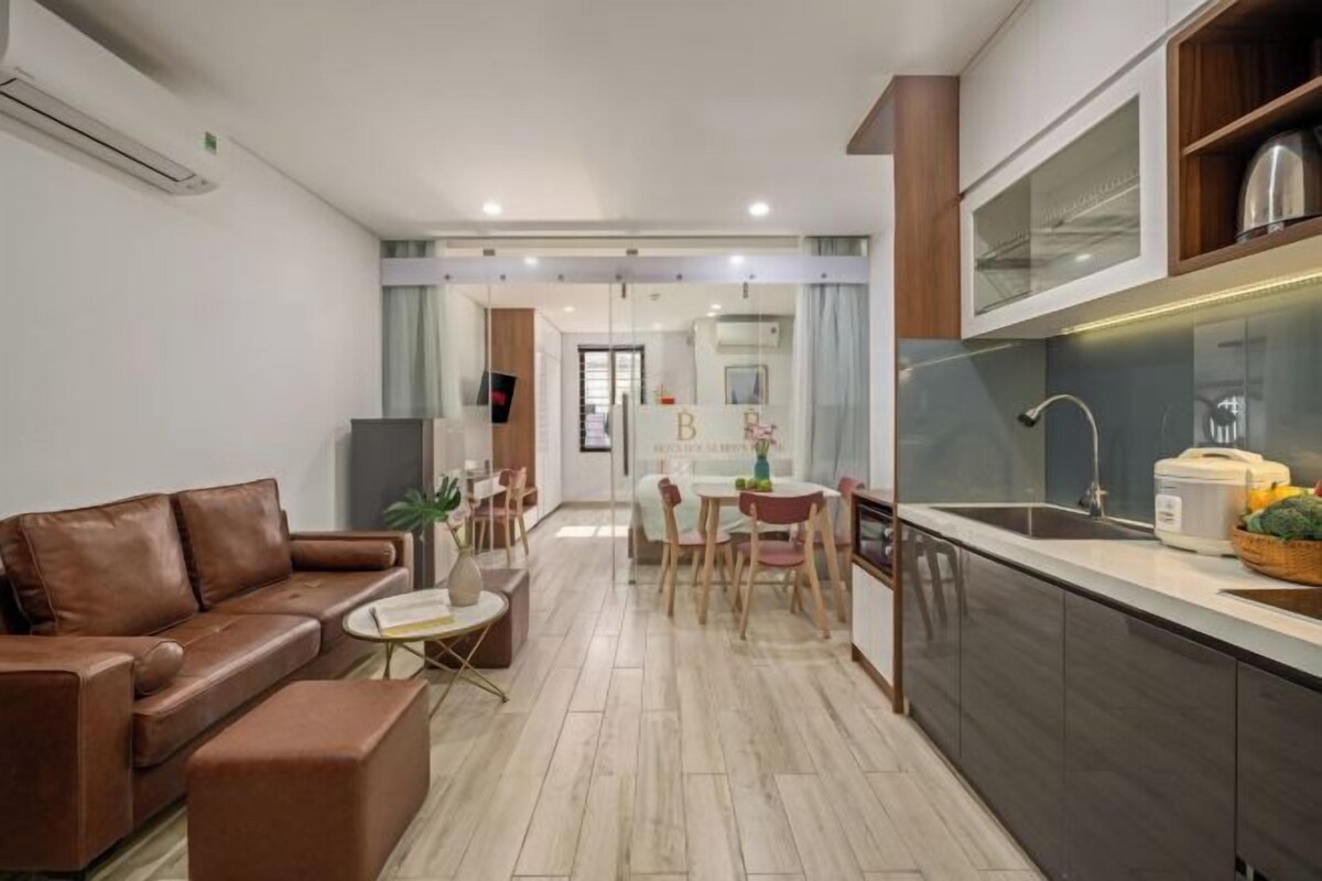 A modern living room with a brown leather sofa, a small coffee table, and a dining area with a wooden table and chairs.