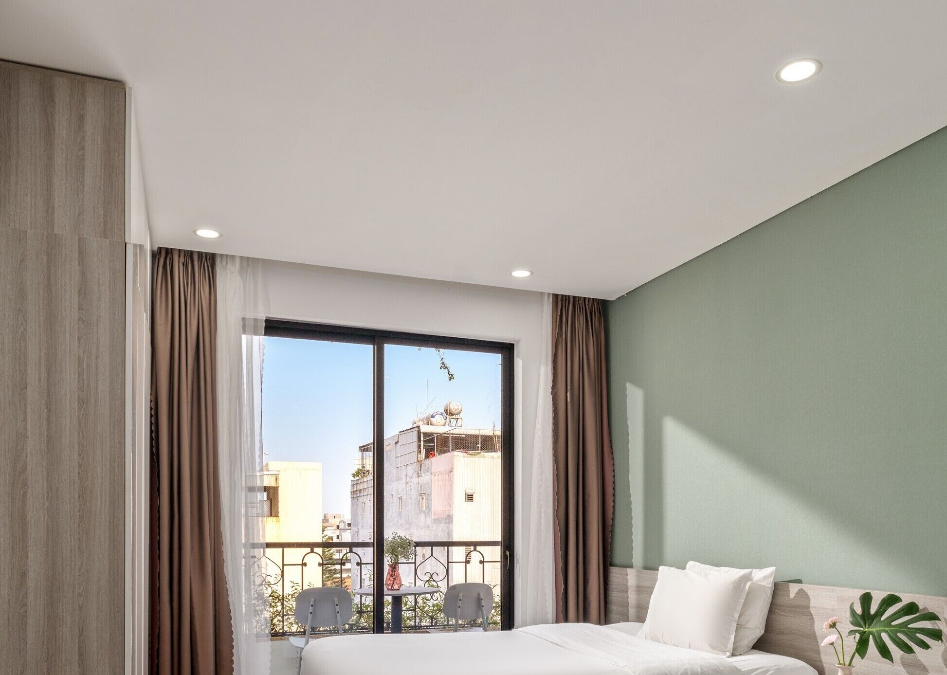 A modern bedroom with a large window, a bed, and a small balcony with chairs.