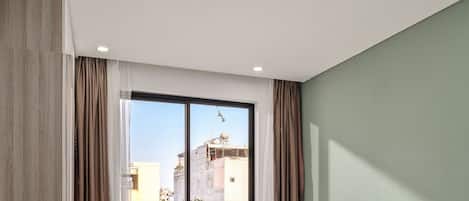 A modern bedroom with a large window, a bed, and a small balcony with chairs.