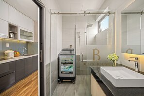 A modern bathroom with a large mirror, a white sink, and a glass shower enclosure. - Ben's House Boutique (Da Nang)