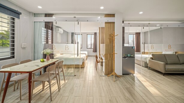 A modern hotel room with a large bed, a dining area with a table and chairs, a sofa, a refrigerator, and a wooden stand. - Ben's House Boutique (Da Nang)