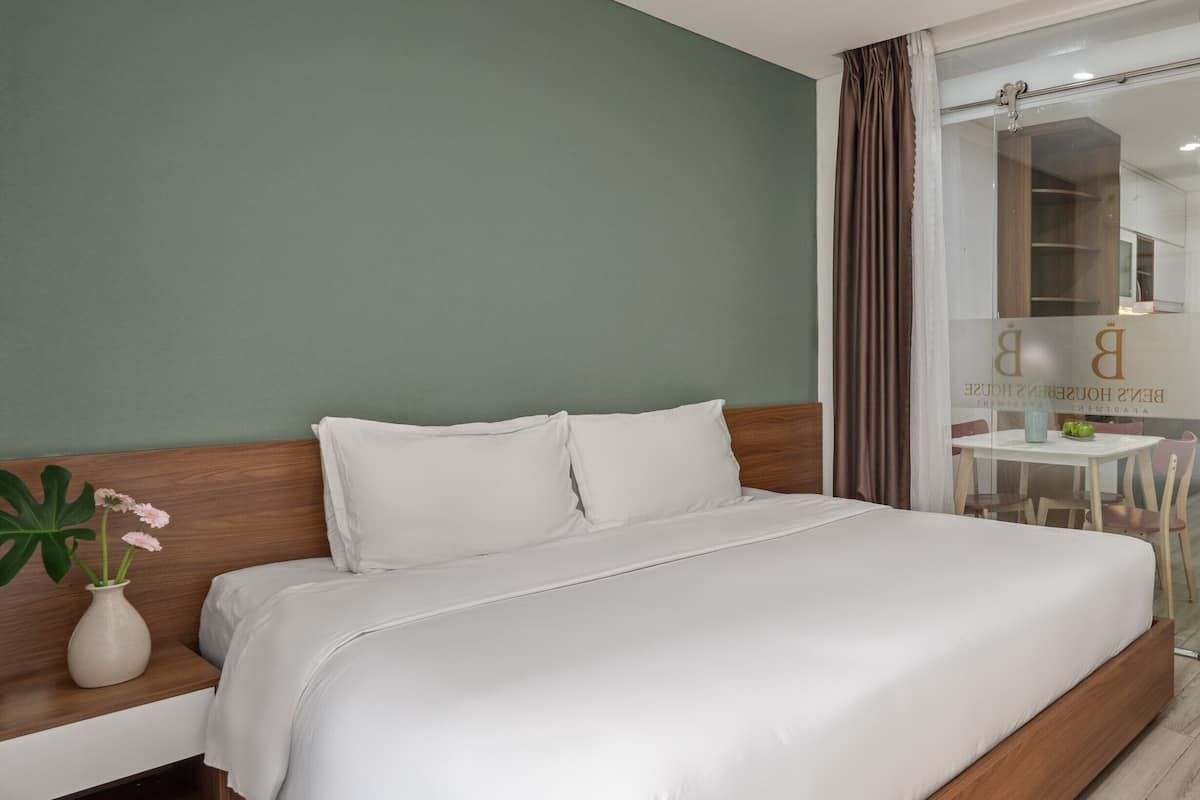 A hotel room with a large bed, a bedside table, a mirror, and a view of the hotel lobby.