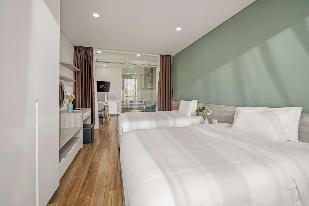 A hotel room with two beds, a TV, a desk, and a bathroom visible through a glass door.