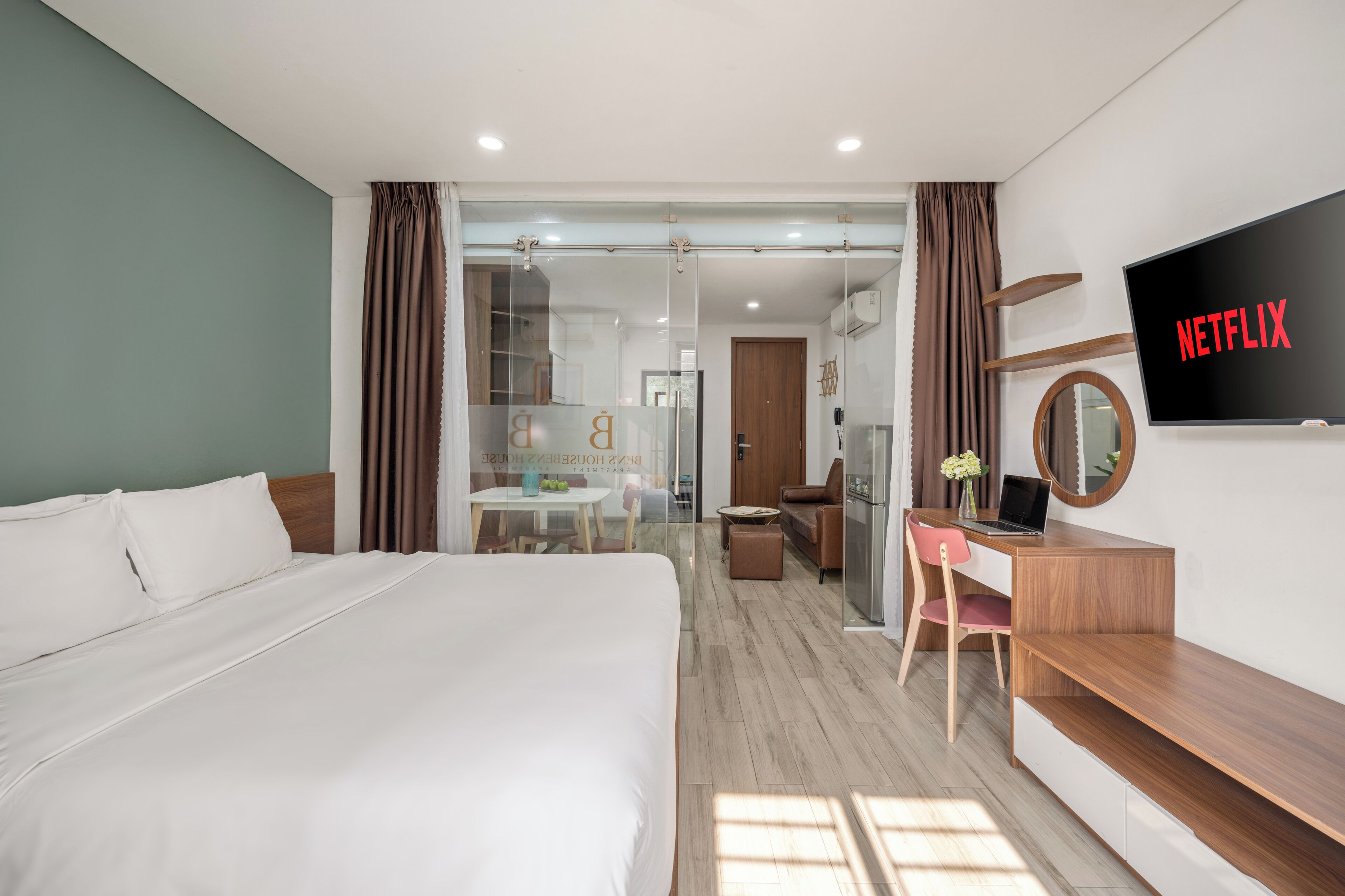 Une chambre d’hôtel avec un grand lit, un bureau avec un ordinateur portable, un téléviseur fixé au mur et une vue sur la chambre adjacente.