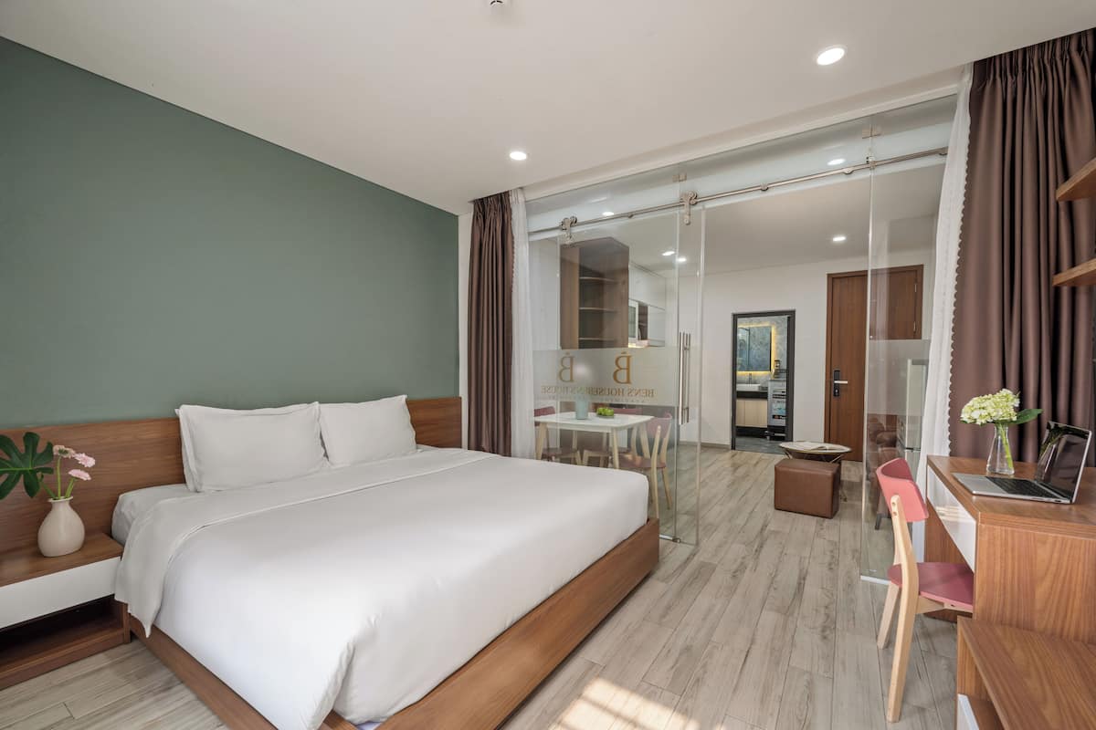 A modern hotel room with a large bed, a desk with a laptop, a chair, and a small table.