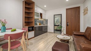 A modern living room with a brown leather sofa, a dining table with pink chairs, and a kitchen area with wooden shelves and a built-in oven. - Ben's House Boutique (Da Nang)