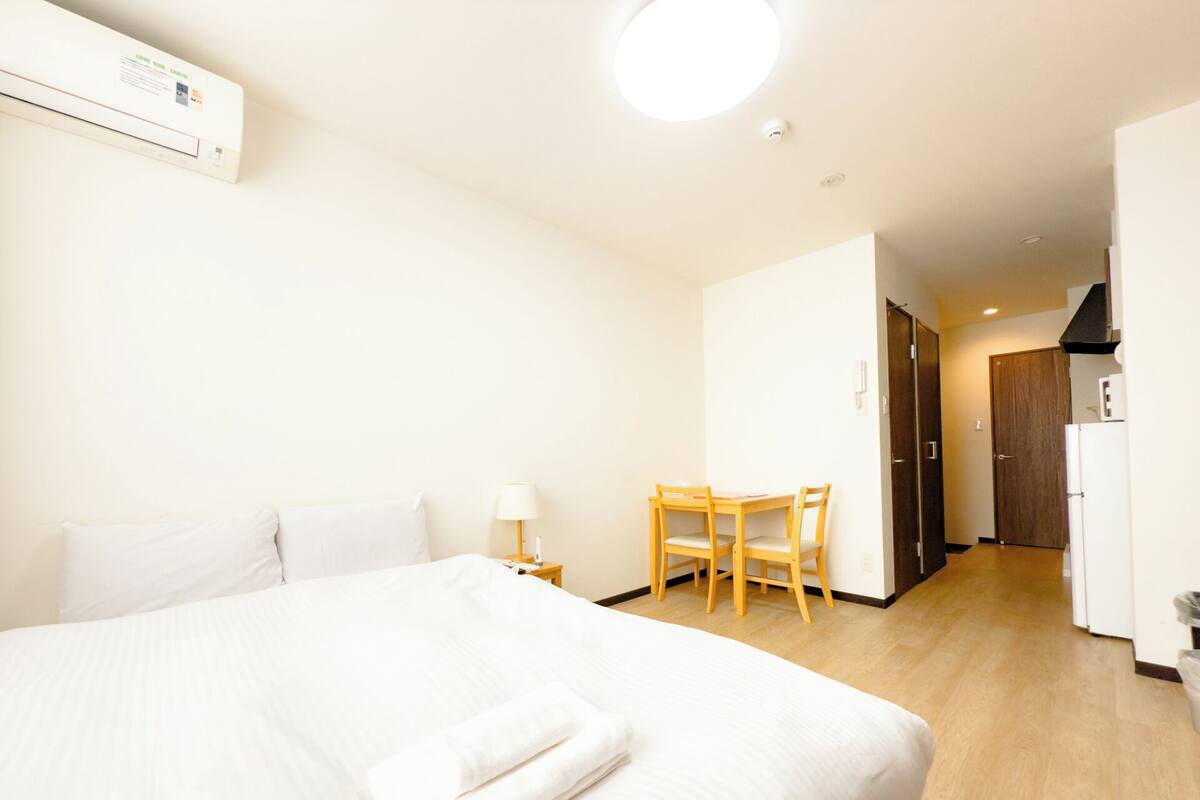 Une chambre d’hôtel avec un grand lit, une petite table avec des chaises, une lampe et une kitchenette.