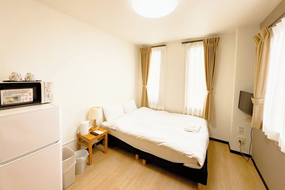 Une chambre d’hôtel équipée d’un lit, d’un bureau avec une lampe, d’un micro-ondes, d’une télévision et d’une poubelle.