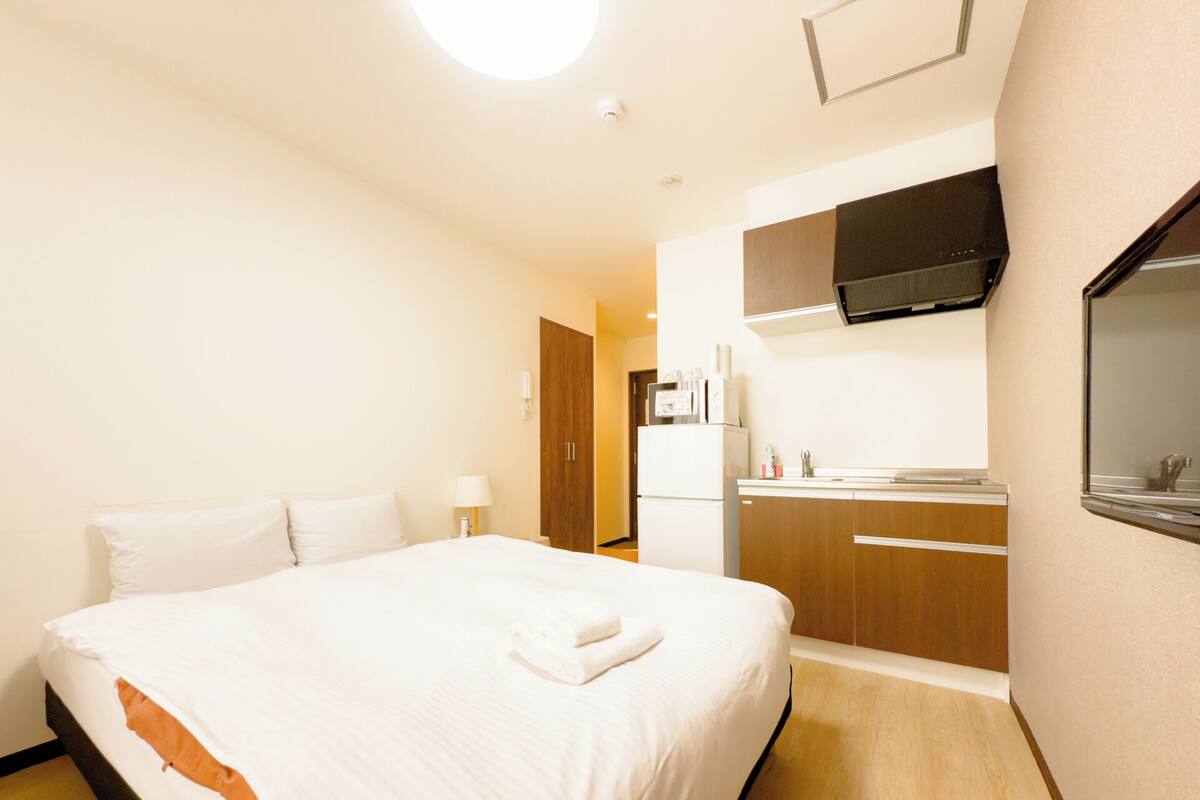Une chambre d’hôtel avec un lit, un téléviseur fixé au mur, une kitchenette et une porte de salle de bain.