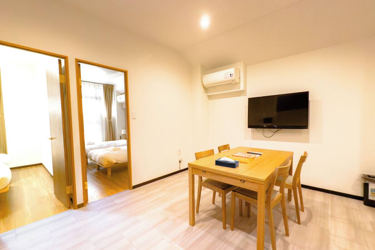 Une chambre d’hôtel avec une table à manger en bois, des chaises, un téléviseur fixé au mur et un lit doté de rideaux.