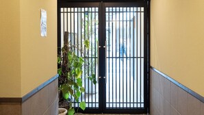 A hallway with a black gate, a potted plant, and a tiled floor. - Hotel SaintFelician Kyoto Shijo Karasuma (Kyoto)