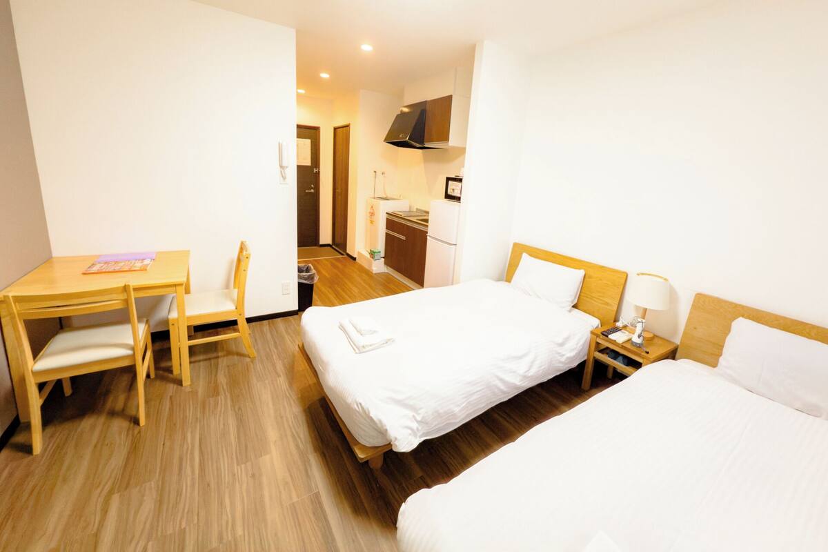 Une chambre d’hôtel avec deux lits, un bureau, une chaise, une table de chevet et une kitchenette.