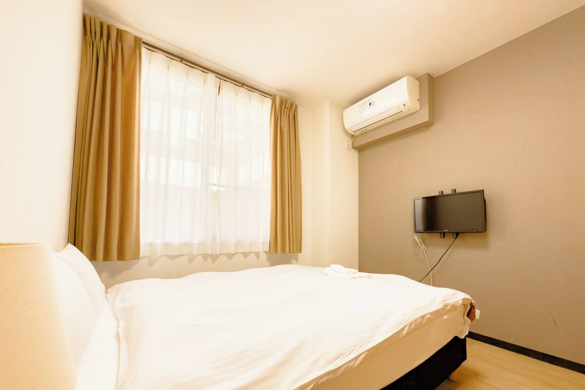 Une chambre d’hôtel équipée d’un lit, de rideaux, d’un climatiseur et d’un téléviseur fixé au mur.