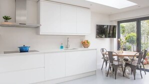 Une cuisine moderne avec des meubles blancs, un pot bleu et un coin repas comprenant une table et des chaises.