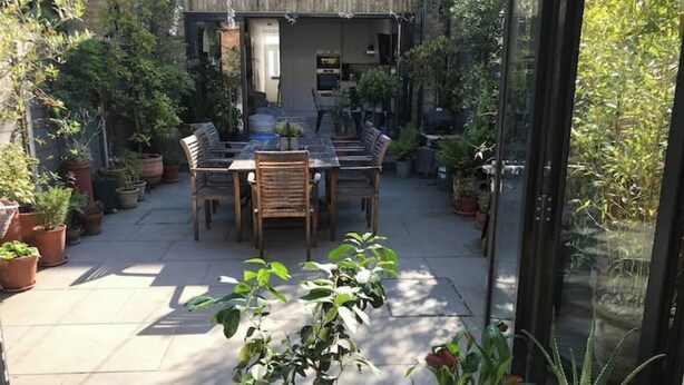 Une terrasse extérieure avec une table et des chaises, entourée de plantes en pot.