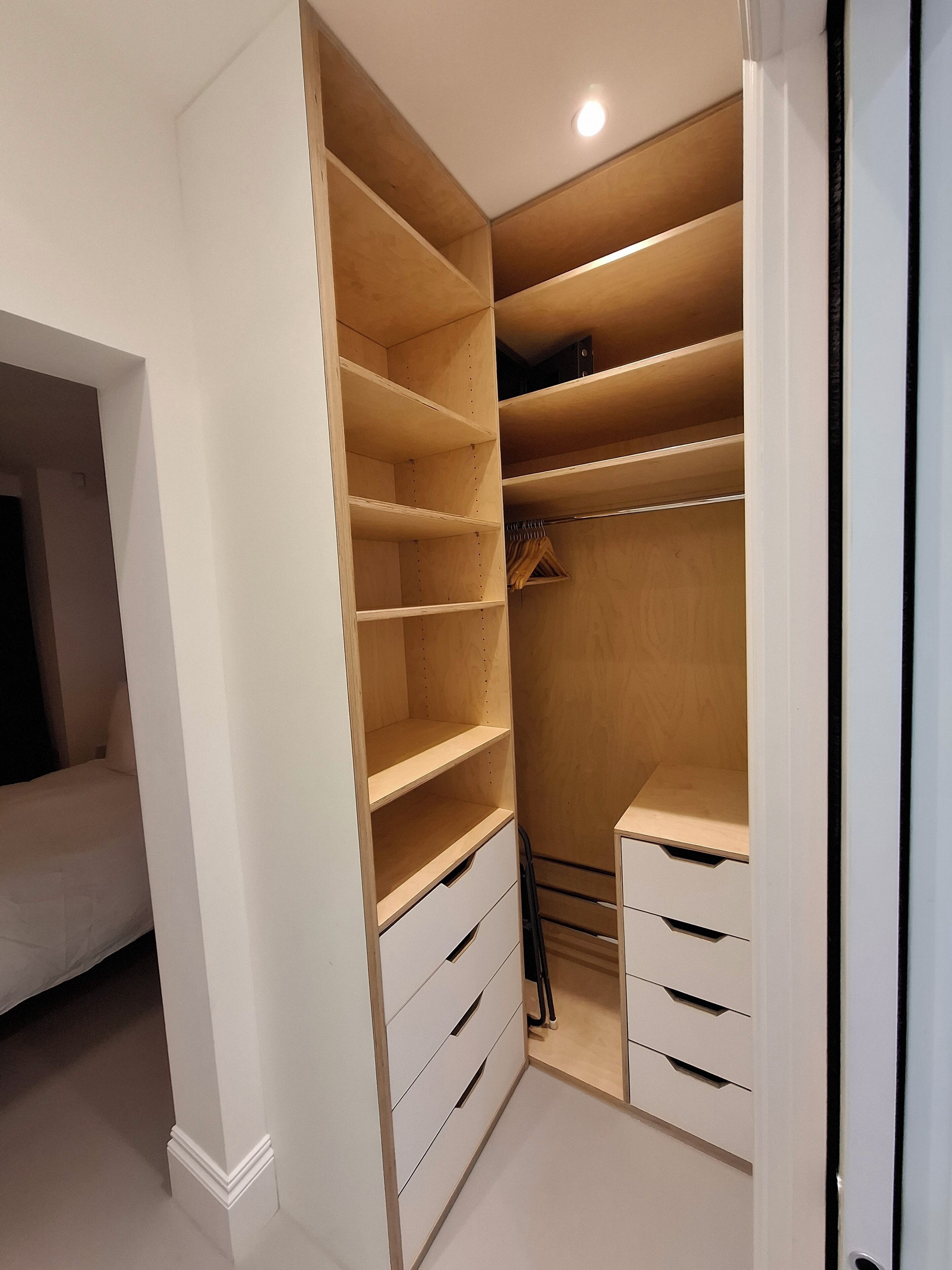 A walk-in closet with multiple shelves and drawers, a hanging rod, and a small seating area.