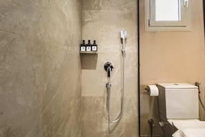 Un baño con ducha, inodoro y estante con artículos de aseo.