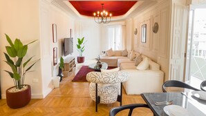 A modern living room with a white sofa, a patterned armchair, a red ceiling, and a chandelier. - Xuru Stays I The 2bdr Crimson Crib @ The Heart Of Heliopolis (Cairo)