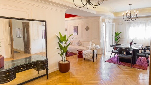 A spacious living room with a large mirror, a dining area with a table and chairs, and a potted plant. - Xuru Stays I The 2bdr Crimson Crib @ The Heart Of Heliopolis (Cairo)