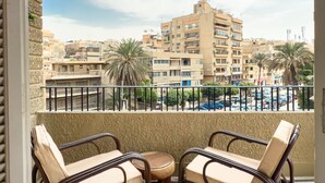 A balcony with two chairs and a small table, overlooking a parking area and buildings. - Xuru Stays I The 2bdr Crimson Crib @ The Heart Of Heliopolis (Cairo)
