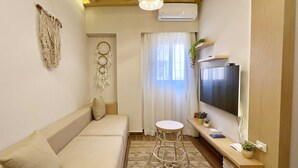 A cozy living room with a sofa, a round stool, a flat-screen TV, and a decorative wall hanging. - Xuru Stays I New Cairo Studios (New Cairo)