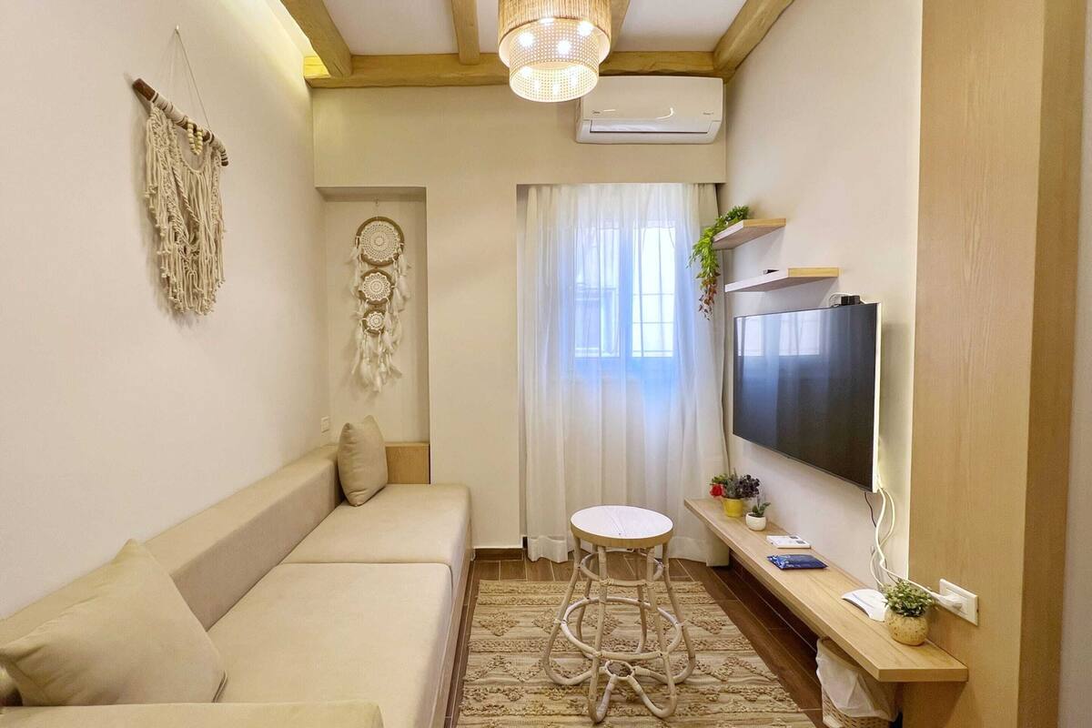 Uma sala de estar aconchegante com um sofá, um banquinho redondo, uma TV de tela plana e um enfeite de parede.
