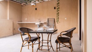 A dining area with a glass table and four wicker chairs, a small sink, and a hanging plant. - Xuru Stays I New Cairo Studios (New Cairo)