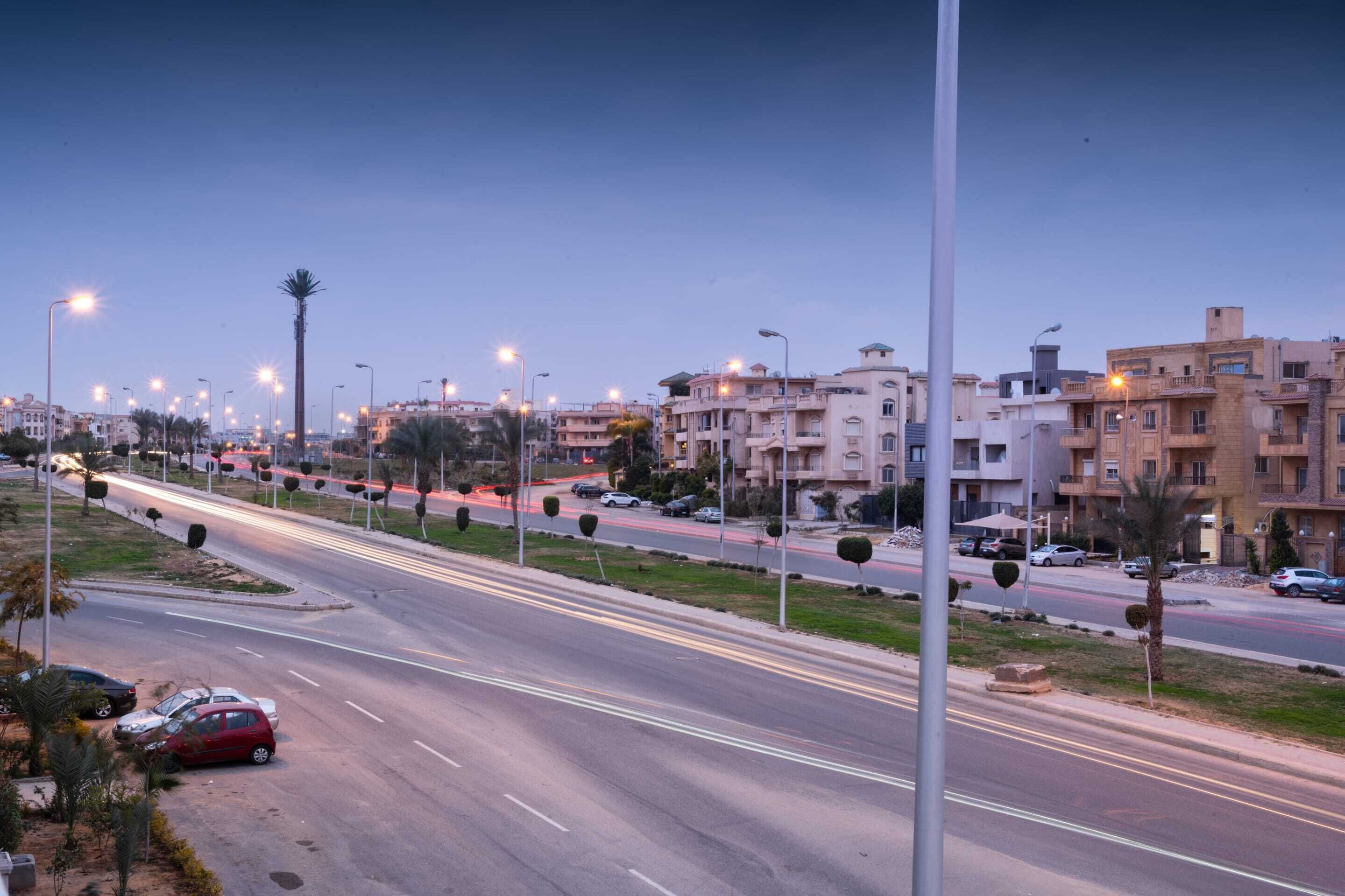 A wide urban road with multiple lanes, lined with streetlights and palm trees.