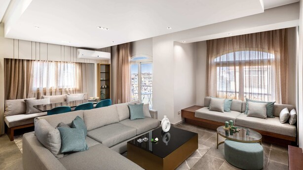 A modern living room with a sectional sofa, a glass coffee table, and a view of the city through large windows. - Xuru Stays I The Sleek & Ritzy 2 BDR 15 min From CAI Airpt (New Cairo)