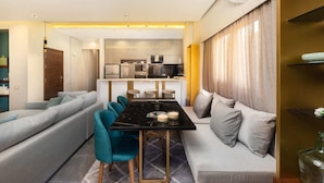 A modern living room with a sofa, teal chairs, and a dining table with candles. - Xuru Stays I The Sleek & Ritzy 2 BDR 15 min From CAI Airpt (New Cairo)