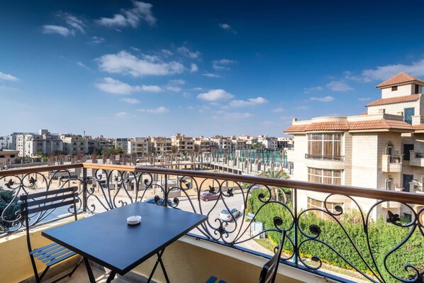 A balcony with a table and bench, overlooking a residential area with buildings and a clear sky. - Xuru Stays I The Sleek & Ritzy 2 BDR 15 min From CAI Airpt (New Cairo)
