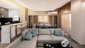 A modern living room with a sofa, a coffee table, and a kitchen area with a counter and stools. - Xuru Stays I The Sleek & Ritzy 2 BDR 15 min From CAI Airpt (New Cairo)