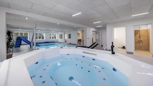 Een modern binnenzwembad met een jacuzzi, ligbedden en een glijbaan.