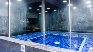 Un bain à remous aux motifs géométriques bleus, entouré de murs de verre offrant une vue sur le paysage urbain.