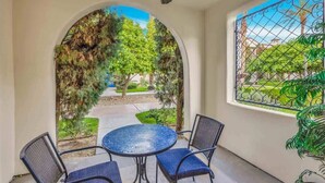 A room with a round table and two chairs, a ceiling fan, and a view through an arched doorway to a garden with trees and a pathway. - Desert Charm B | Studio Legacy Villa (La Quinta)