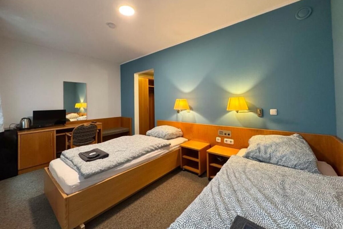 Une chambre d’hôtel avec deux lits simples, un bureau, une chaise, une télévision et une armoire.