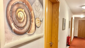 A hallway with a large painting of shells on the wall, a wooden door, and a red carpeted floor. - AR Airport Hotel Rüsselheim (Ruesselsheim)