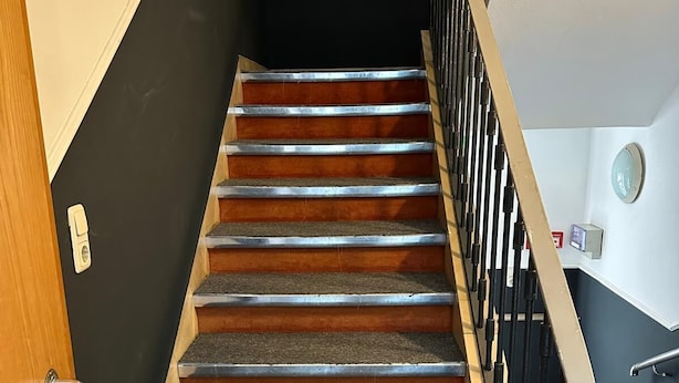 A staircase with wooden steps and metal railings, leading to a landing with a wall-mounted clock. - AR Airport Hotel Rüsselheim (Ruesselsheim)