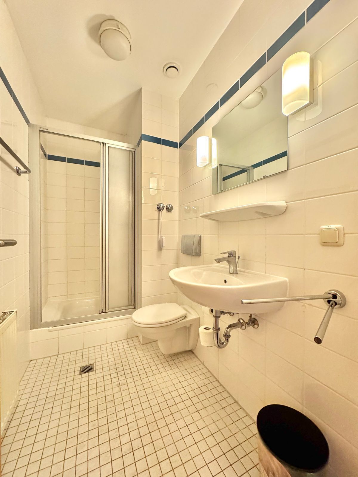 Ein modernes Badezimmer mit Duschkabine aus Glas, Toilette und Waschbecken mit Spiegel darüber.