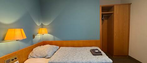 A single bed with a wooden headboard, two wall-mounted lamps, and a wooden wardrobe in a room with blue walls.