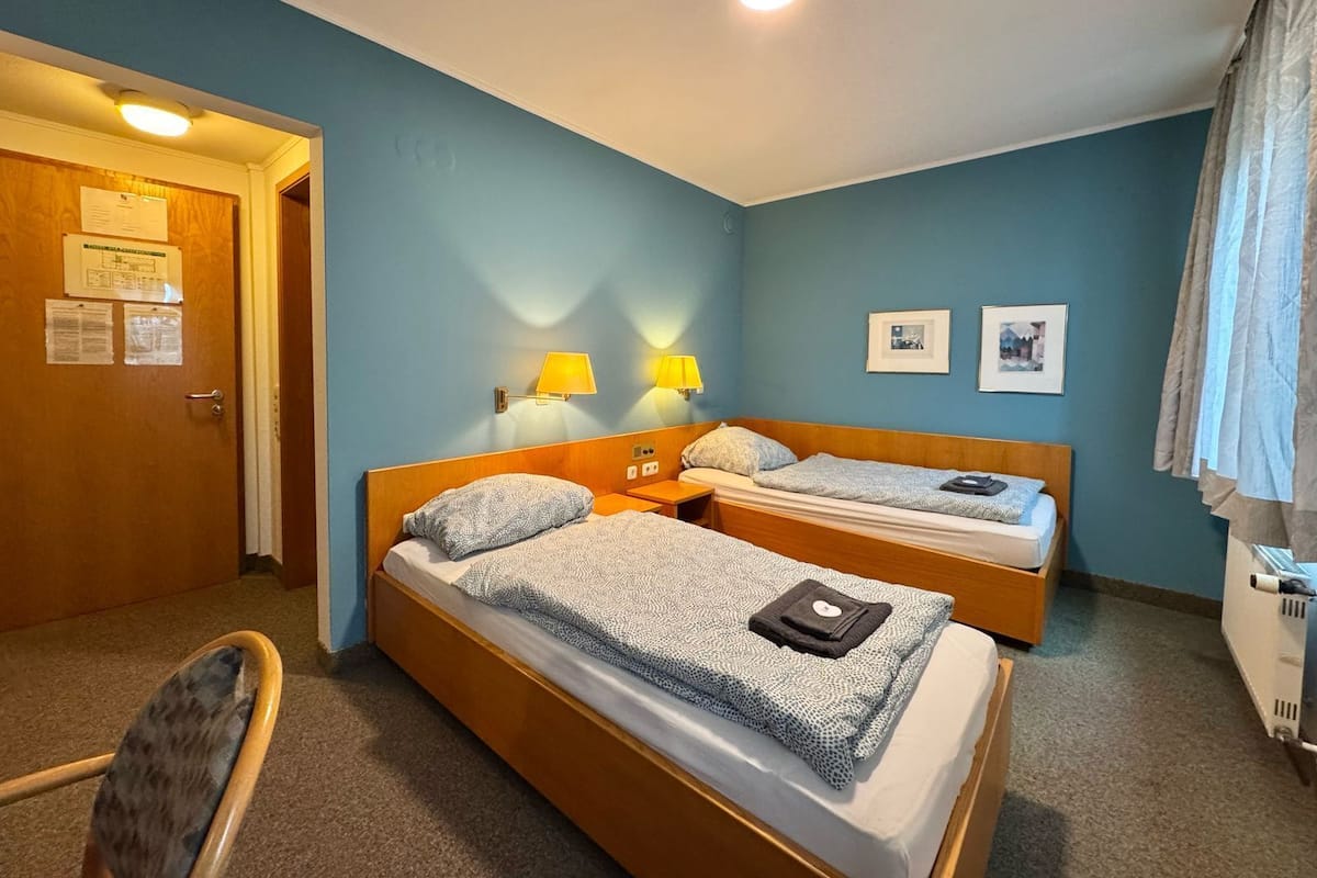 A hotel room with two single beds, a wooden door, a chair, and a radiator.