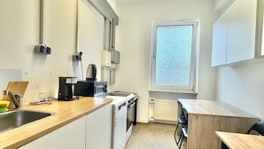 A modern kitchen with white cabinets, a wooden countertop, a built-in oven, and a window providing natural light. - AR Airport Hotel Rüsselheim (Ruesselsheim)