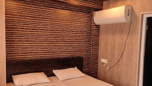 A bedroom with a wooden headboard, a checkered bedspread, and an air conditioning unit mounted on the wall. - Hotel Koyal Mandi (Mandi)