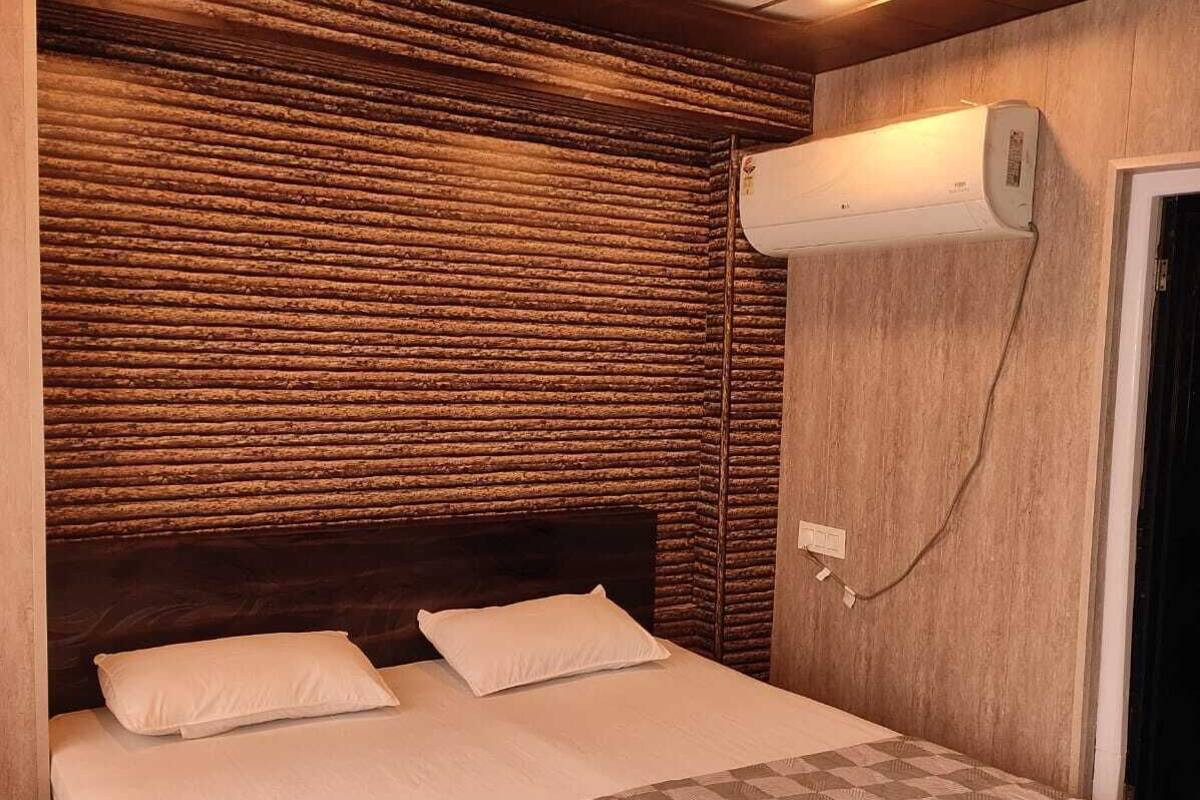 A bedroom with a wooden headboard, a checkered bedspread, and an air conditioning unit mounted on the wall.