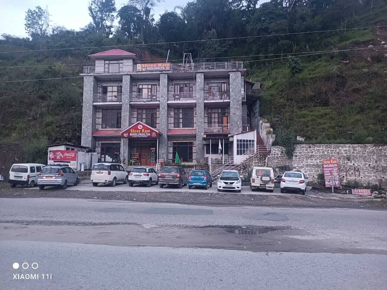 A multi-story building with a sign for "Shree Ram Bhopjalaya" on the ground floor. Several cars are parked in front.