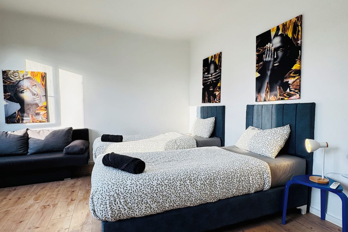 Een moderne slaapkamer met een groot bed, een kleinere zithoek en twee kunstwerken aan de muur.