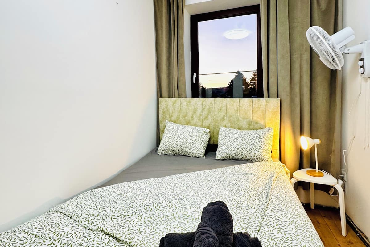 Een hotelkamer met een bed, een raam, een nachtkastje met lamp en uitzicht op buiten.