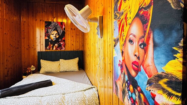 Une pièce en bois avec un lit, un ventilateur et un grand tableau accroché au mur.