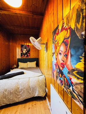 Une pièce en bois avec un lit, un ventilateur et un grand tableau accroché au mur.