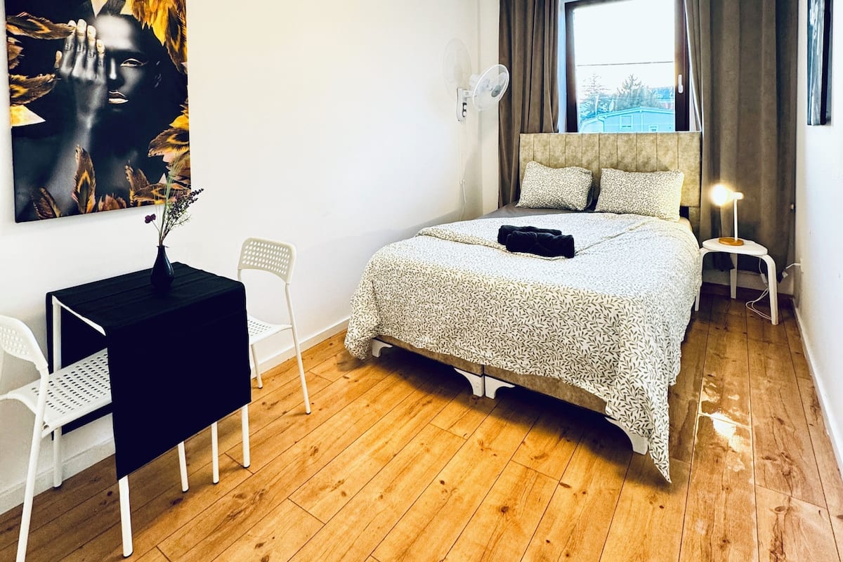 Een slaapkamer met een bed, een bureau, een stoel, een raam en een plafondlamp.